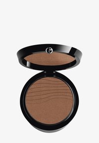 Compact de bronceador con estuche redondo negro, que presenta un patrón ondulado en la superficie del polvo bronceador. Se cierra con un seguro clic.