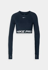 Musta pitkähihainen lyhyt urheilu toppi, jossa valkoinen Nike-logo rinnassa ja "NIKE PRO" -teksti joustavassa vyötärössä.