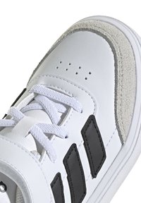 Sneaker bianco con tomaia in pelle sintetica, accenti in suede, strisce nere laterali e lacci bianchi. Collo imbottito e suola in gomma testurizzata.
