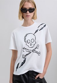 Vit bomulls-T-shirt med svart skalle och korslagda ben, klomärken, korta ärmar och avslappnad passform.