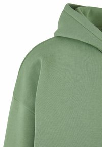 Hoodie en coton vert avec une texture douce, présentant une grande capuche et une coupe décontractée. Le tissu semble légèrement extensible et lisse.