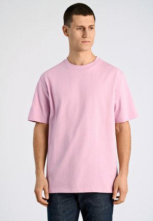 Roze katoenen T-shirt met korte mouwen en een ronde hals. Geko combined met donkerblauwe spijkerbroek, op een effen achtergrond. Glad materiaal, ontspannen pasvorm.