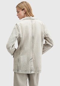 Giacca in denim grigio chiaro con vestibilità rilassata, dettagli di cucitura visibili e colletto classico. Presenta maniche lunghe e tasche laterali.