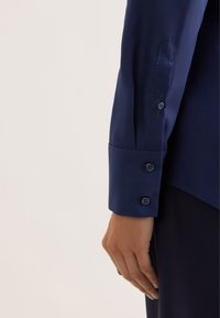 Navy button-up shirt sleeve featuring a smooth texture, three buttons at the cuff, and a tailored fit with a structured design.