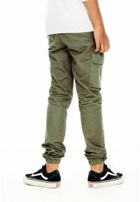 Groene cargo broek met elastische boorden, zijzak en een ongeforceerde pasvorm. Draagt met zwart-witte Vans sneakers.