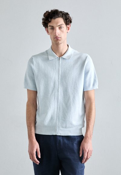 Polo azzurro chiaro a maniche corte con zip, realizzato in tessuto a maglia testurizzata, con colletto classico e orlo dritto, abbinato a pantaloni navy.
