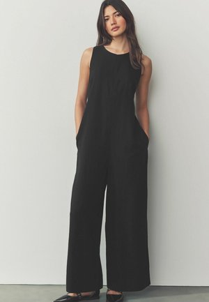 Combinaison noire sans manches avec des jambes larges, poches latérales et un tissu lisse et léger. Design simple et épuré avec un col rond.