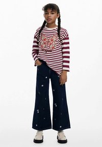 Gestreiftes Langarmshirt mit Schmetterlingsgrafik, kombiniert mit weiten, dunkelblauen Denim-Hosen mit bunten, bestickten Blumendetails.