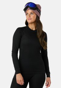 Schwarzes langärmeliges Thermoshirt mit geripptem Design, kombiniert mit schwarzen Leggings. Eine hellpinkfarbene Strickmütze und Skibrille runden das Outfit ab.