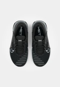 Baskets de sport noires avec une tige en maille, des accents texturés et un logo blanc. Présentent une semelle plate et un système de laçage traditionnel.