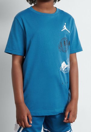 Niño con camiseta azul de Jordan con logo Jumpman blanco y diseños gráficos, combinado con pantalones cortos deportivos azules con detalles blancos.