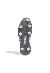 Silonová podrážka sportovní obuvi s hladkým šedým povrchem, výrazným vzorem dezénu a šesti bílými plastovými hroty pro lepší trakci.