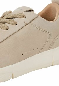 Baskets en cuir beige avec une texture lisse, bout rond, lacets contrastants et perforations minimales sur le côté. Semelle en caoutchouc blanche.
