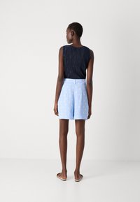 Navy pleated sleeveless top paired with light blue shorts featuring white polka dots, set against a neutral background.