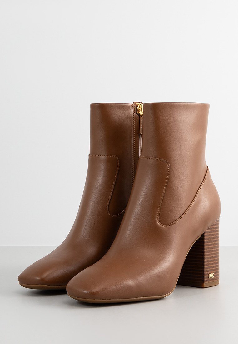 Une paire de bottines en cuir marron mi-mollet avec des orteils arrondis, des talons carrés, des fermetures éclair sur les côtés et un logo doré discret sur le talon.