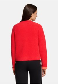 Czerwony, puszysty sweter o pudełkowym kroju i krótkiej długości. Posiada okrągły dekolt i długie rękawy z mankietami w jaśniejszym odcieniu.