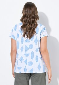 Camiseta blanca de manga corta con patrones geométricos azules, que incluyen líneas y formas. Tejido suave con un corte relajado.