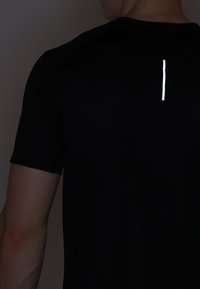 Camiseta deportiva negra con una franja vertical reflectante en la parte posterior, mangas cortas y una textura de malla transpirable.