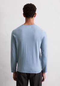 Hellblaues Langarmshirt mit rundem Halsausschnitt, weicher Textur und leicht tailliertem Schnitt, mit Raglanärmeln und glattem Rücken.