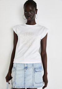 Hvid bomulds-t-shirt med korte ærmer og glitrende teksttryk. Kombineret med en lys denimnederdel med to frontlommer.