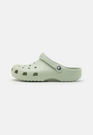 Sabot vert clair à enfiler avec des trous de ventilation, semelle texturée et bride de talon réglable avec un badge rond à logo.