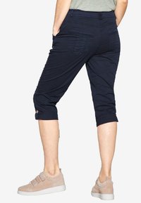 Pantalons navy raccourcis avec une texture douce, poignets retroussés et poches arrière, associés à des baskets beige clair. Design minimaliste.