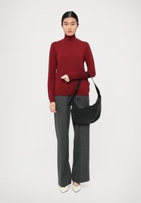 Burgunderfarget turtleneck-genser, grå vidbukse og en svart vevd håndveske. Modellen har på seg hvite spisse sko. Enkel og moderne design.