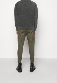 Szara bluza z prążkowanymi mankietami, zestawiona z oliwkowymi, zwężanymi spodniami. Czarne botki za kostkę o fakturowanym wykończeniu dopełniają stylizację.