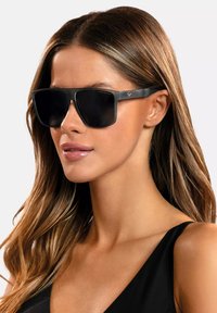 Okulary przeciwsłoneczne z czarnymi ramkami z poliwęglanu i ciemnymi soczewkami, charakteryzujące się prostokątnym kształtem i teksturowanymi detalami na zausznikach.