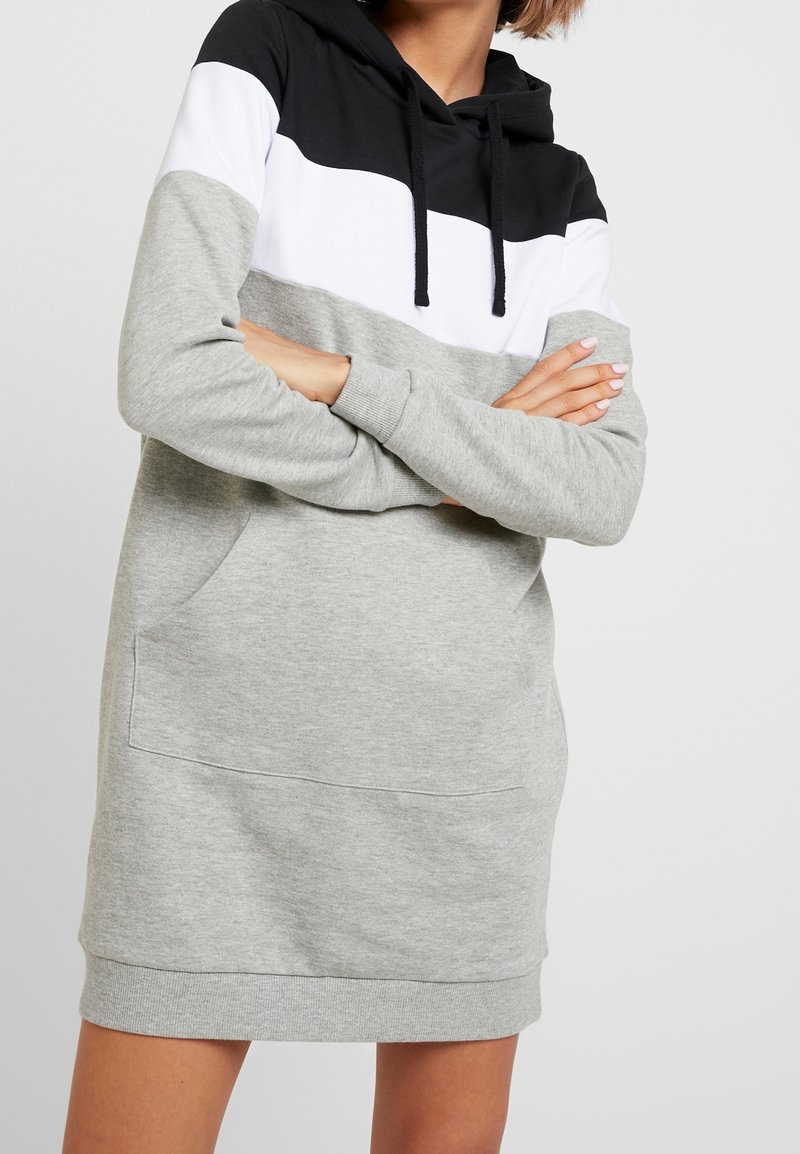 Robe pull à capuche avec un design en bloc de couleurs présentant des sections noires, blanches et grises. Fabriquée en mélange de coton doux, elle comprend une poche avant.