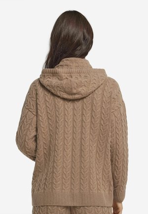 Brązowy, sweter z warkoczowym splotem, z pojemnym kapturem. Posiada ściągacze przy mankietach i u dołu. Materiał wygląda na miękki i teksturowany, zapewniając przytulne wrażenie.
