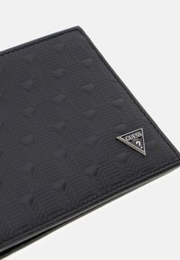 Czarny portfel wykonany z teksturowanego materiału, ozdobiony geometrycznym wzorem oraz trójkątnym metalowym akcentem logo w dolnym rogu.