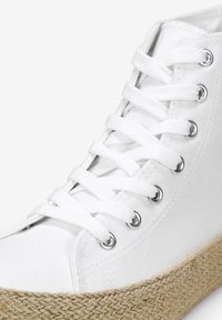 Zapatilla alta de lona blanca con cordones planos blancos, ojales de metal y una suela intermedia de yute texturizado. Detalles de costura a lo largo de los bordes.