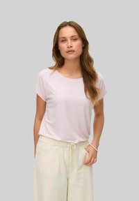 Lyserød kortærmet t-shirt med rund halsudskæring og afslappet pasform, parret med lysebeige bukser med snøre i taljen. Blød, glat stoftekstur.
