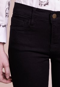 Jeans de mezclilla negra con un diseño ajustado, estilo de cinco bolsillos, costuras ligeras y un botón de latón con la marca "FRAME" en la bragueta.