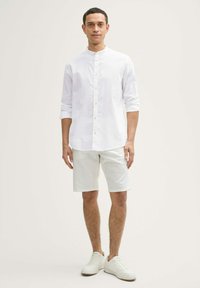 Camică albă cu mânecă lungă, cu închidere cu nasturi, asortată cu pantaloni scurți deschiși la culoare și adidași albi. Design simplu și curat, realizată dintr-un material moale.