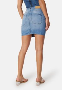 Minigonna di jeans azzurro chiaro con design aderente, due tasche posteriori e orlo leggermente sfrangiato. Abbinata a sandali con tacco a blocco trasparente.