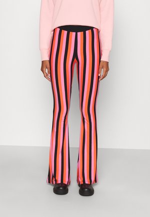 Persoon die een hoge taille wijde broek met verticale roze, oranje, rode en zwarte strepen draagt, gecombineerd met zwarte schoenen en een lichtroze top.