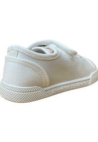 Sneakers de lona blanca con suela de goma texturizada, cinta de velcro y detalles de costura sutiles. Nombre de la marca “Blanditos by Cris’s” grabado en el lateral.