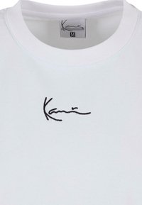 Valge puuvillane sportswear, millel on ümmargune kaelus ja must tikitud allkiri esiküljel. Suure silt näitab "M".