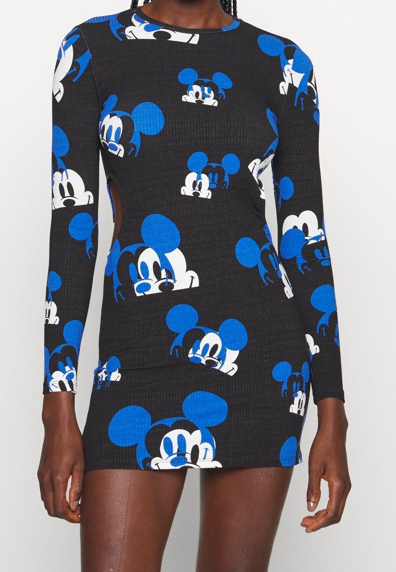 Robe mini noire cintrée à manches longues avec un motif de visages de Mickey Mouse bleus et blancs sur le tissu, portée par une personne à la peau foncée.
