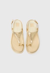 Sandali metallici dorati con design a t-strap, dettagli in metallo circolari e una soletta beige chiaro con bordi texturizzati.