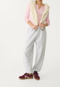 Lichtroze geribd langarmshirt, crèmekleurig faux fur-vest, grijze ontspannen sweatpants en bordeauxrode sneakers met crèmekleurige accenten en rubberen zolen.