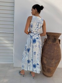 Rochie albă cu modele botanice albastre, cu spate decupat și fustă fluidă. Asortată cu mules cu toc argintii și o vază din ceramică maro.