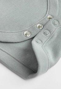 Body in cotone grigio chiaro con scollatura rotonda, dotato di tre bottoni a pressione metallici sulla spalla per facilitare l'inserimento.