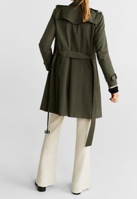 Olivengrüner Trenchcoat mit tailliertem Schnitt, großem Kragen und Gürtel in der Taille. Verfügt über lange Ärmel und eine glatte Stofftextur.