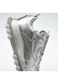 Silberner Sportschuh mit eleganter metallischer Oberfläche, gepolsterter Zunge, strukturierten Akzenten und robustem Gummisohle mit distinctem Profil.