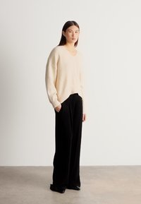 Krémový sveter s výstrihom do V v kombinácii s čiernymi širokými nohavicami. Sveter má voľný strih a textúrovanú látku; nohavice majú dĺžku po zem.