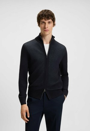Maglione zip-up blu scuro con colletto alto, polsini e orlo a coste. Texture lavorata a maglia con dettagli di pattern sottili e zip argentata.