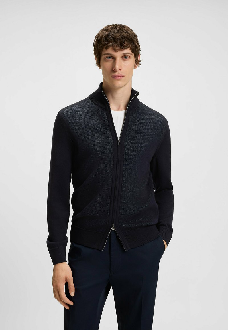 Dunkelblauer Reißverschluss-Pullover mit hohem Kragen, gerippten Bündchen und Saum. Stricktextur mit dezentem Musterdetail und silbernem Reißverschluss.